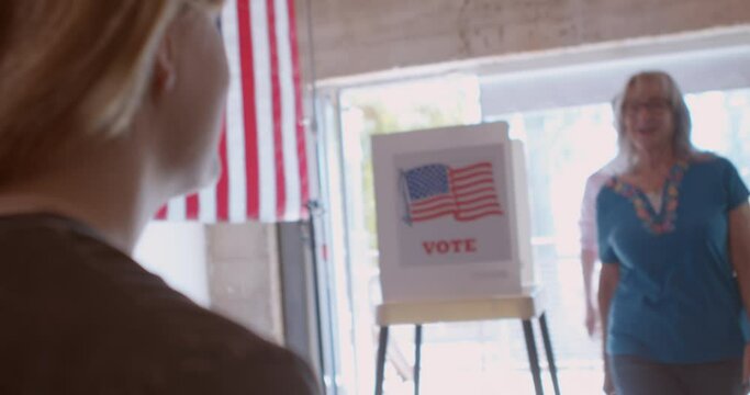 A young female poll worker processing voters at a polling station draped with American flags. 