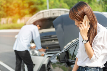 young woman with smartphone by the damaged car after a car accident, making a phone call and for...
