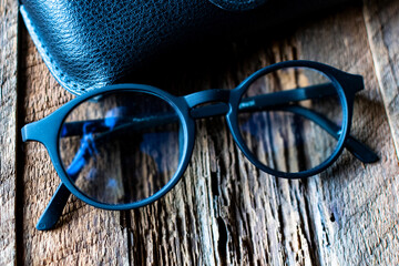 round optical glasses with a case in black plastic frames on textured wood.