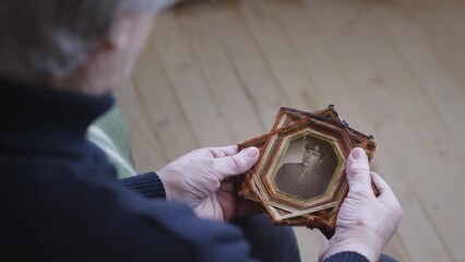 A senior woman cradles an old framed photo of a soldier, capturing a moment of reflection and remembrance.