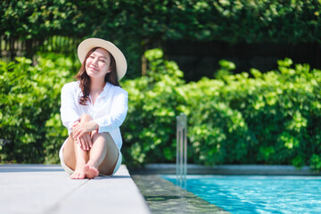Portrait image of a woman with hat sitting by the swimming pool