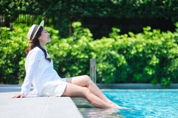 Portrait image of a woman with hat sitting and soaking legs by the swimming pool