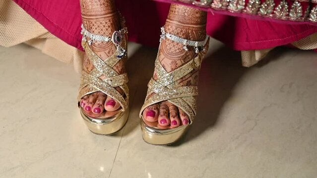 Beautiful bride showing her bridal sandals with silver payal on her legs, with bridal Mehndi henna design on her legs , wearing a beautiful bright lehenga