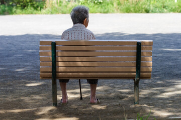公園の日陰のベンチに座る高齢者の後ろ姿