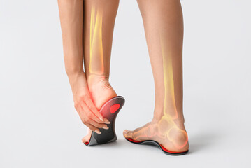 Woman fitting orthopedic insole on light background