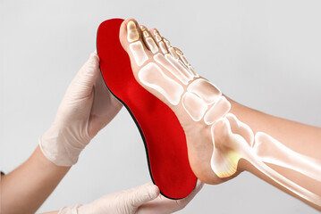 Doctor fitting orthopedic insoles to female legs on light background