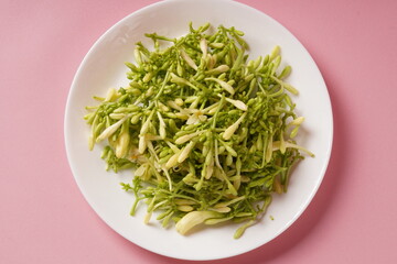 A pile of fresh, green, raw papaya flowers (Carica papaya), with mostly unopened buds, arranged on a white plate and photographed against a pink background.
