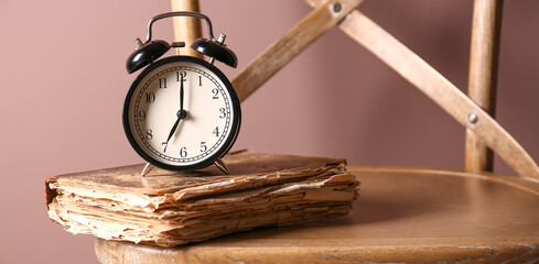 Alarm clock and old book on chair against color background