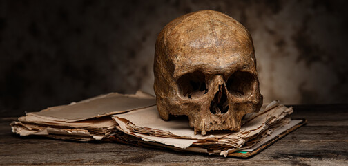Human skull with book on table against dark background