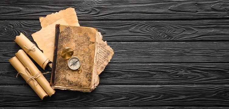 Old book with compass and scrolls on dark wooden background with space for text