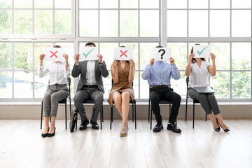 Young people holding paper sheets with different marks while waiting for job interview in office