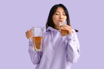 Beautiful Asian woman drinking juice on lilac background