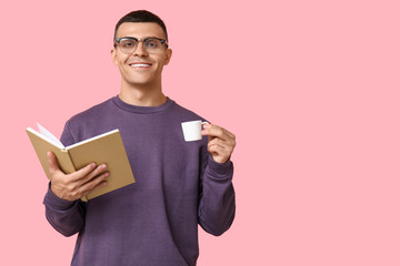 Handsome young man reading book and drinking coffee on pink background