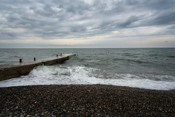 Stormy Black Sea on the Sochi coast and a concrete breakwater on a city beach on a summer day with clouds, Sochi, Krasnodar Territory, Russia