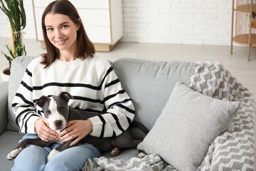 Beautiful young woman with cute staffordshire terrier puppy sitting on sofa at home