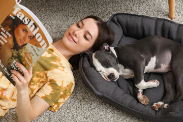 Beautiful young woman with cute staffordshire terrier puppy reading magazine on floor at home