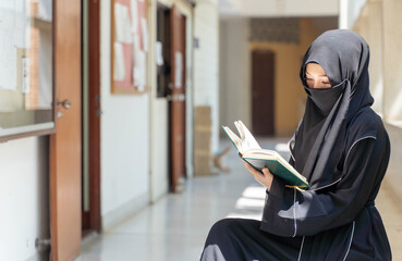 Closeup a beautiful Muslim students wearing traditional clothes are intently reading Quran in the...