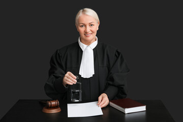 Mature female judge with stamp and document at table on black background