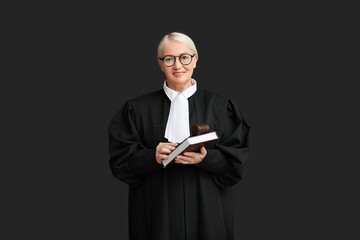Mature female judge with book and gavel on black background