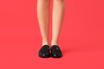 Legs of young woman in stylish black shoes on red background