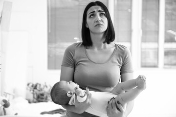 Sad young woman with her baby suffering from postnatal depression in bedroom