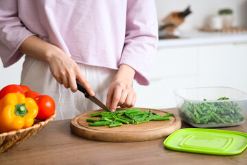 Woman cutting green beans for freezing on wooden table in kitchen
