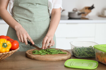 Woman cutting green beans for freezing on wooden table in kitchen