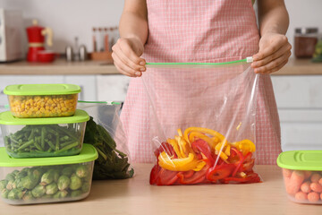 Woman holding plastic bag with bell pepper for freezing at wooden table