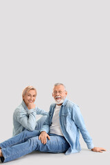 Mature couple in denim clothes sitting on light background