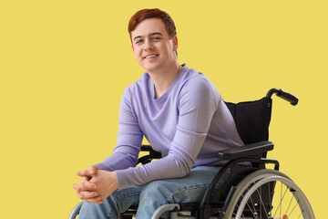 Young man in wheelchair on yellow background