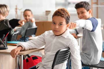 Bullied little African-American boy sitting in classroom