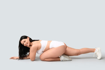 Body positive woman in underwear sitting on light background