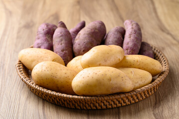 Raw potatoes and purple sweet potatoes in basket on wooden background, Food ingredient