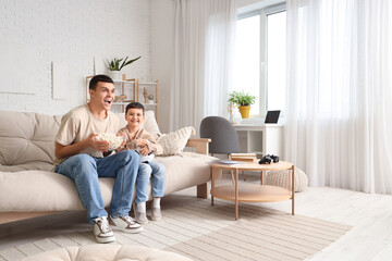 Obraz premium Happy father and his little son with popcorn watching football game at home
