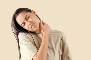 Young woman suffering from neck pain on beige background, closeup