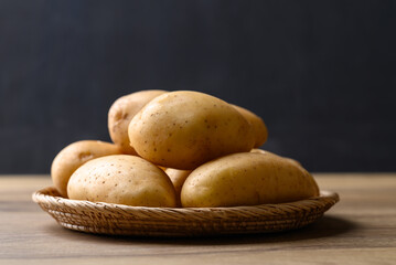 Raw potatoes in basket on wooden table with black background, Food ingredient