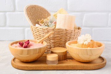 Wooden board with spa accessories and cosmetics on table against light brick wall