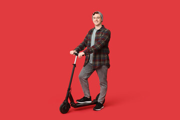 Young man with modern electric kick scooter on red background