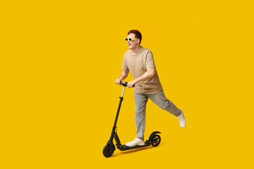 Young man riding modern electric kick scooter on yellow background