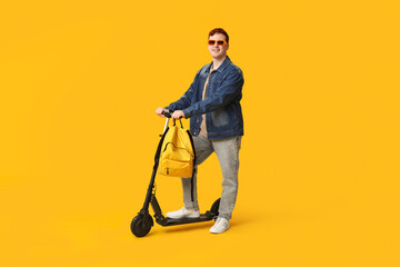Happy young man with modern electric kick scooter on yellow background