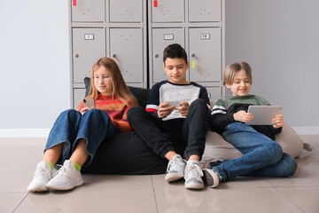 Little pupils using gadgets near locker at school