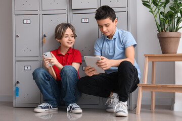 Little schoolboys using gadgets near locker at school