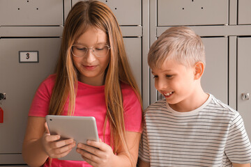 Little pupils using tablet computer near locker at school