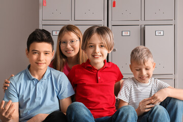 Happy little pupils sitting near locker at school