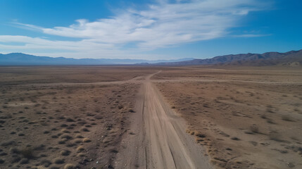 A dirt road leads to mountains on the horizon under a clear blue sky.