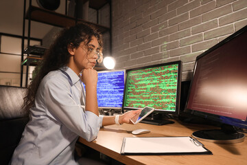 Female African-American programmer with tablet computer working in office at night