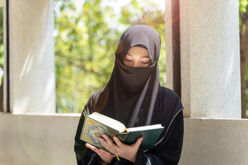 Closeup a beautiful Muslim students wearing traditional clothes are intently reading Quran in the...