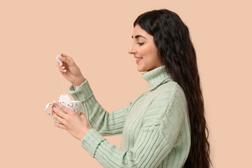 Beautiful young woman with cup of hot tea on beige background