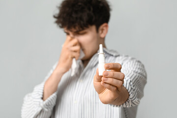 Young man with nasal drops and tissue on grey background. Allergy concept