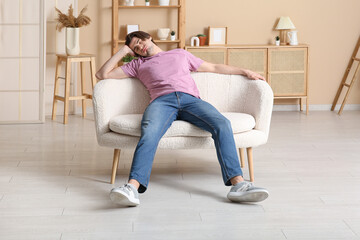 Weary young man sitting on sofa at home